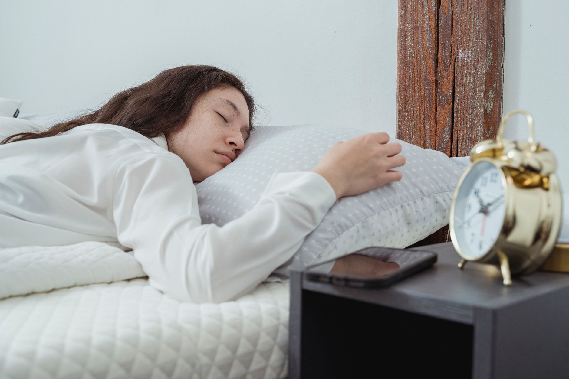 Photo-realistic shot of a woman looking at her phone alarm clock with a determined expression, ready to get out of bed.